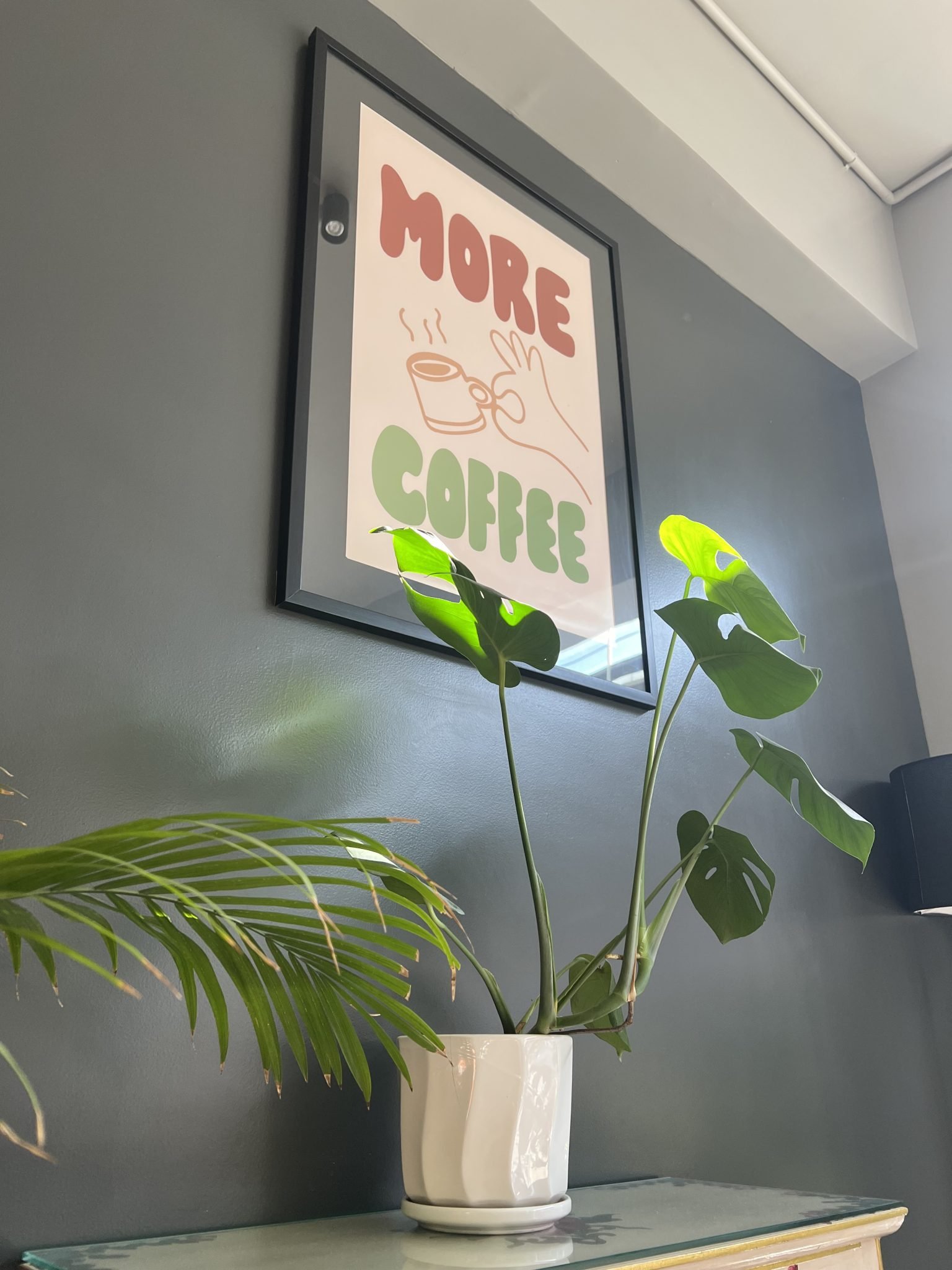Monstera and palm in white pots beneath a framed print